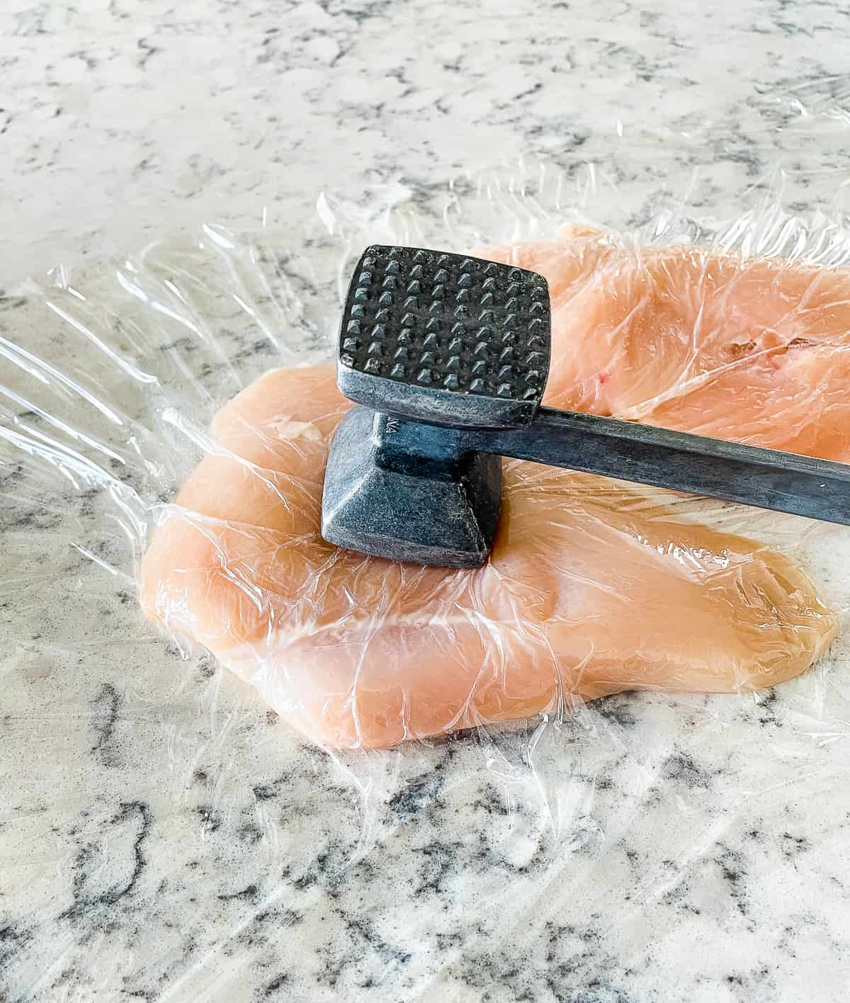 chicken breast being pounded between pieces of plastic wrap