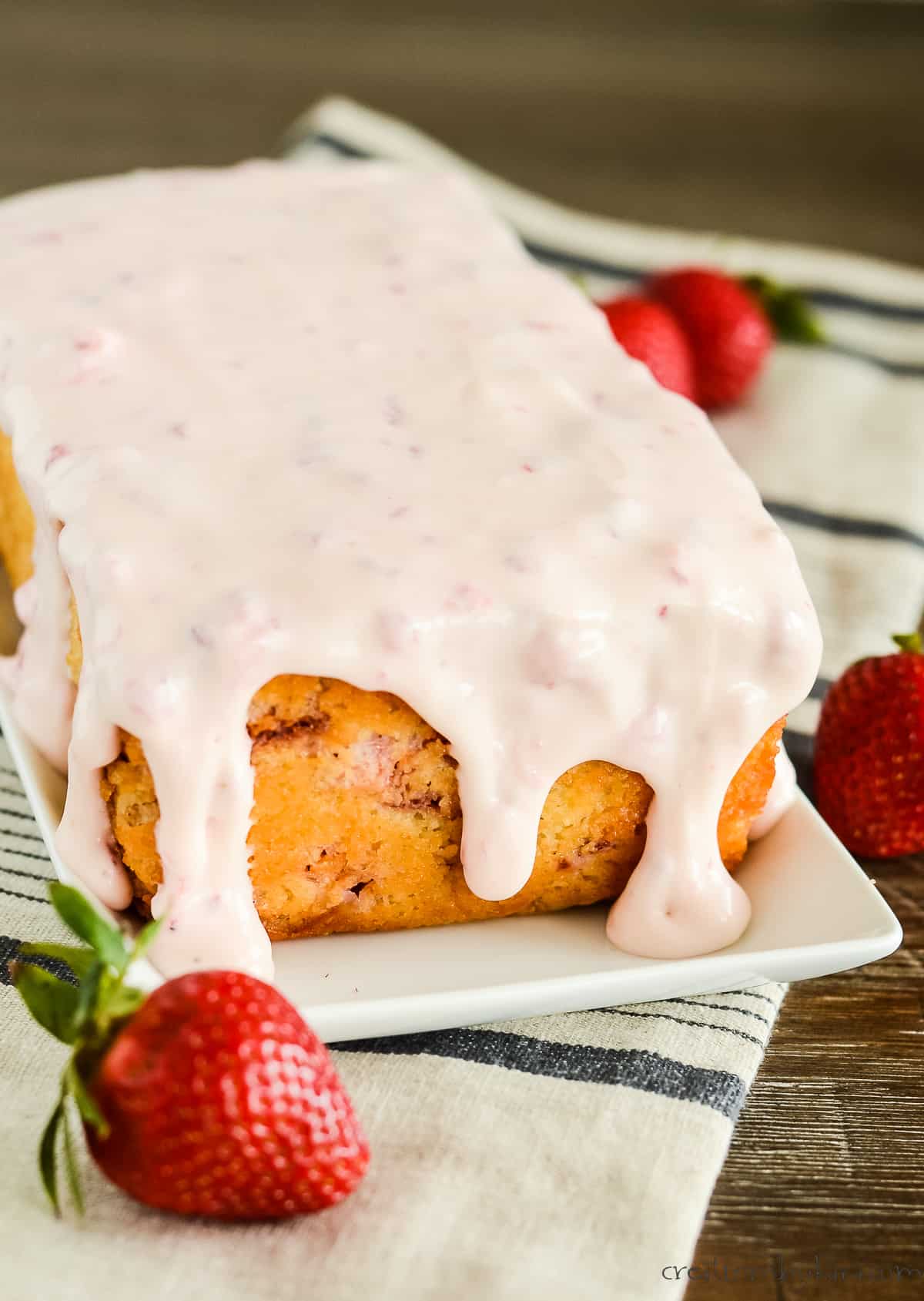 strawberry pound cake on a tray with strawberry cream cheese glaze dripping down the sides