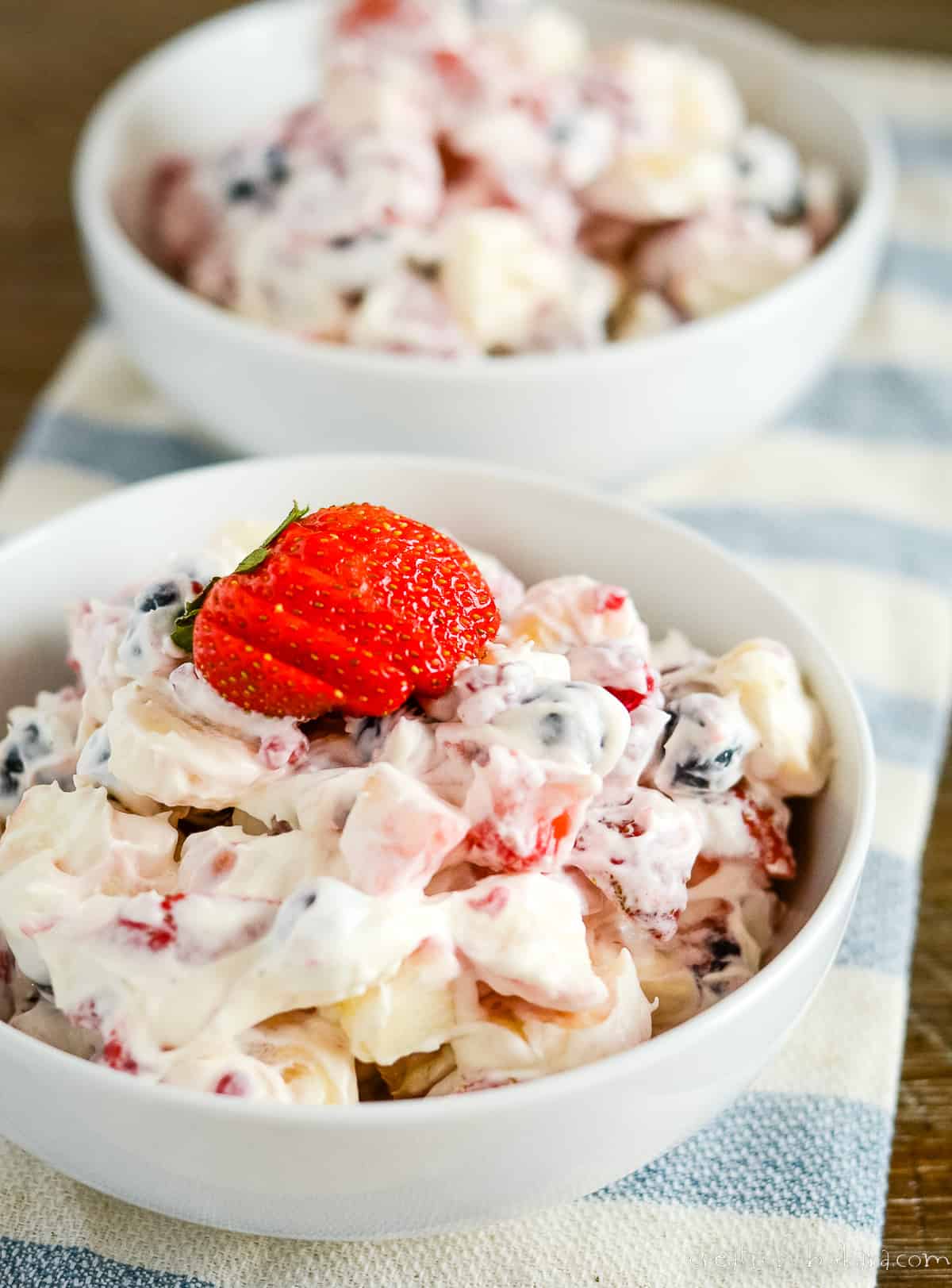 two bowls of cheesecake fruit salad on a striped kitchen towel