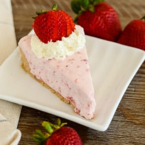 no bake strawberry cheesecake slice garnished with whipped cream and sliced strawberries