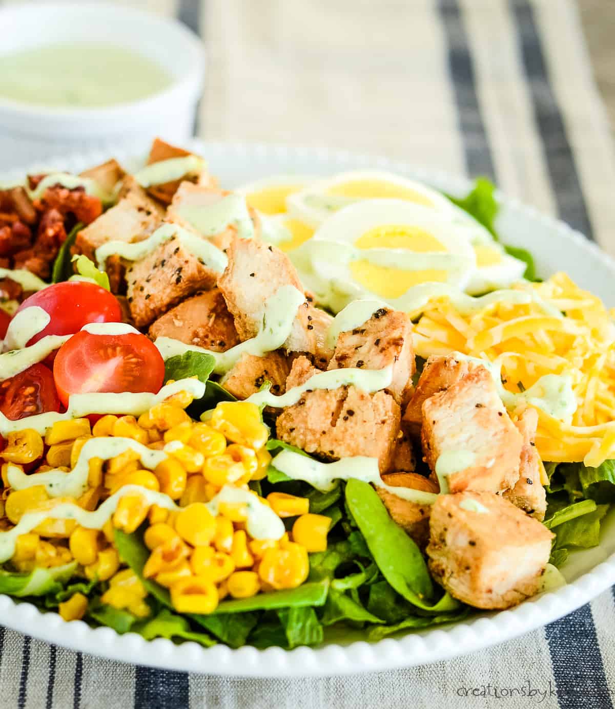 plate of cobb chicken salad with dressing in the background