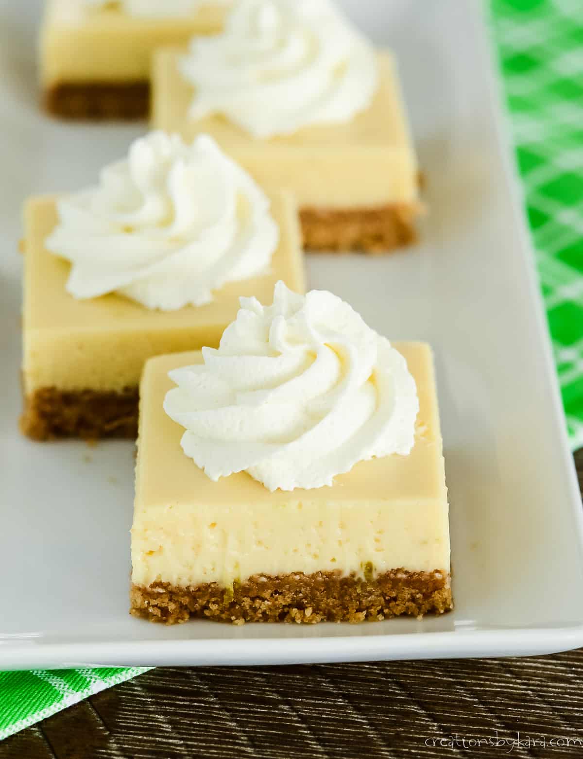 four key lime bars on a white tray sitting on a lime green kitchen towel