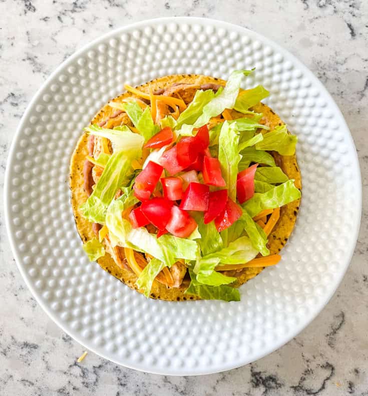 tostada with shredded chicken, refried beans, cheese, lettuce, and tomatoes