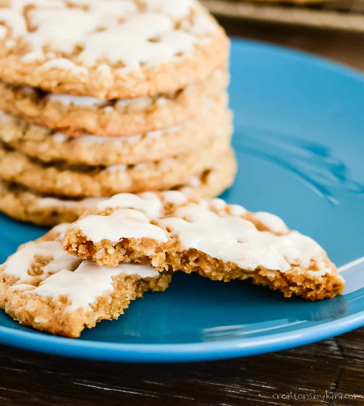 close up of iced oatmeal cookie broken in half with a stack of cookies in the background