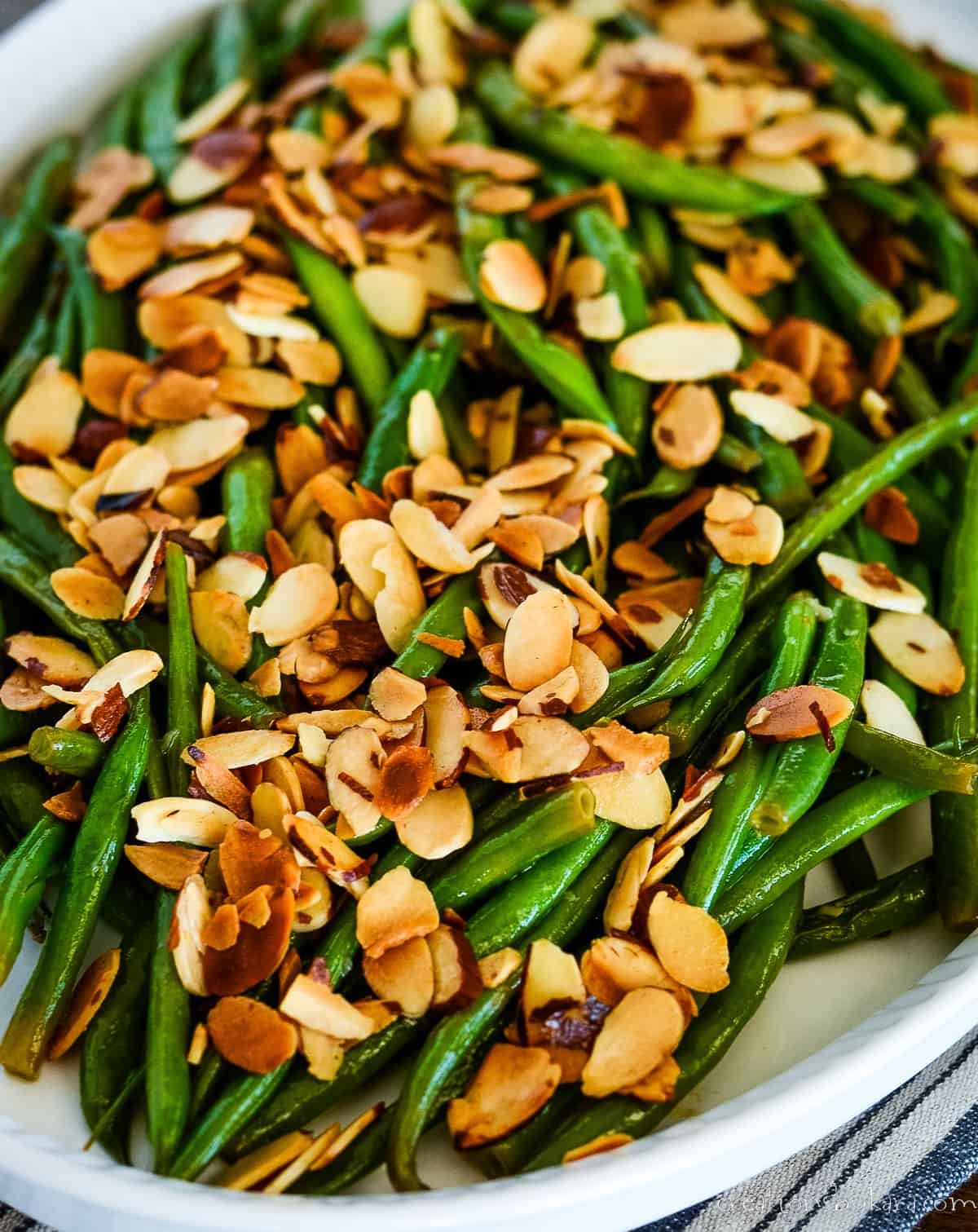 close up of almondine green beans in a white serving dish
