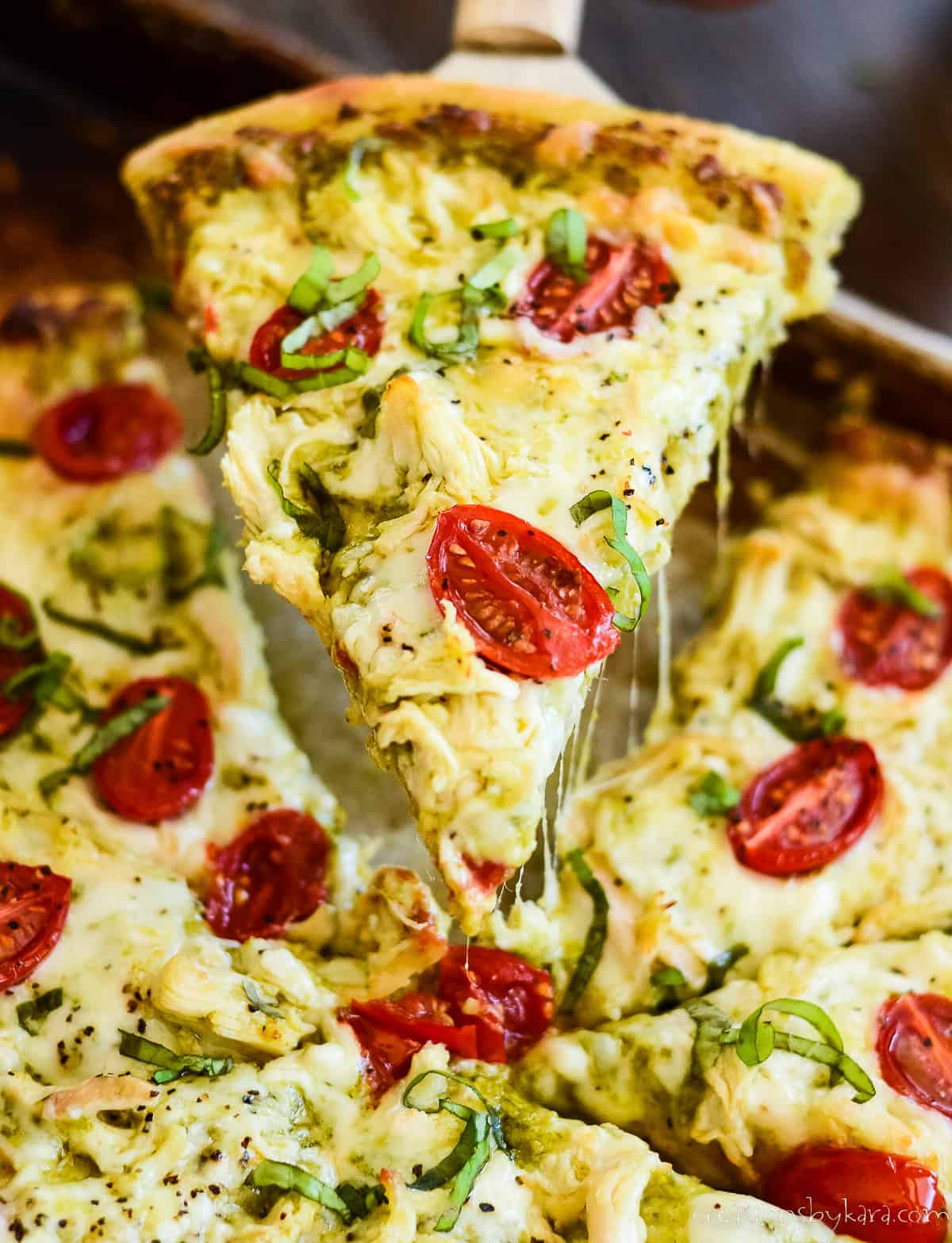 slice of chicken pesto pizza being lifted from the pan