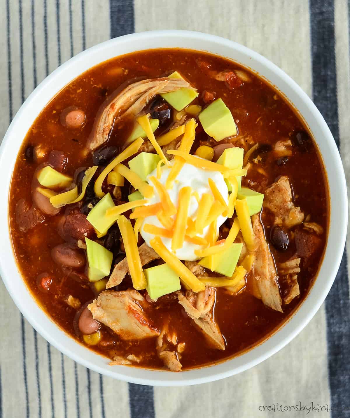 overhead shot of bowl of taco chicken soup with sour cream, cheddar, and avocado