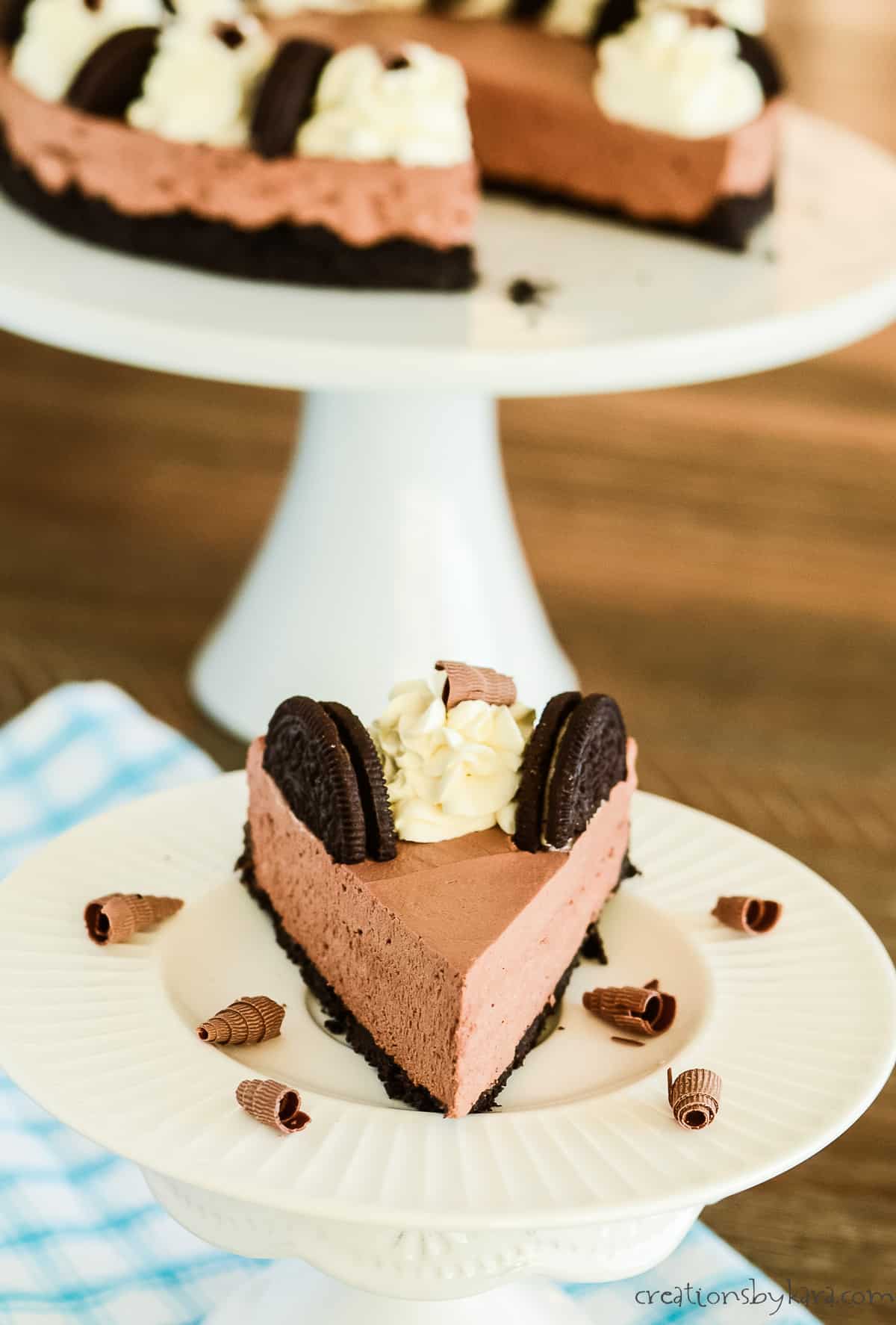 slice of chocolate mousse cake on a plate with a whole sliced cake in the background