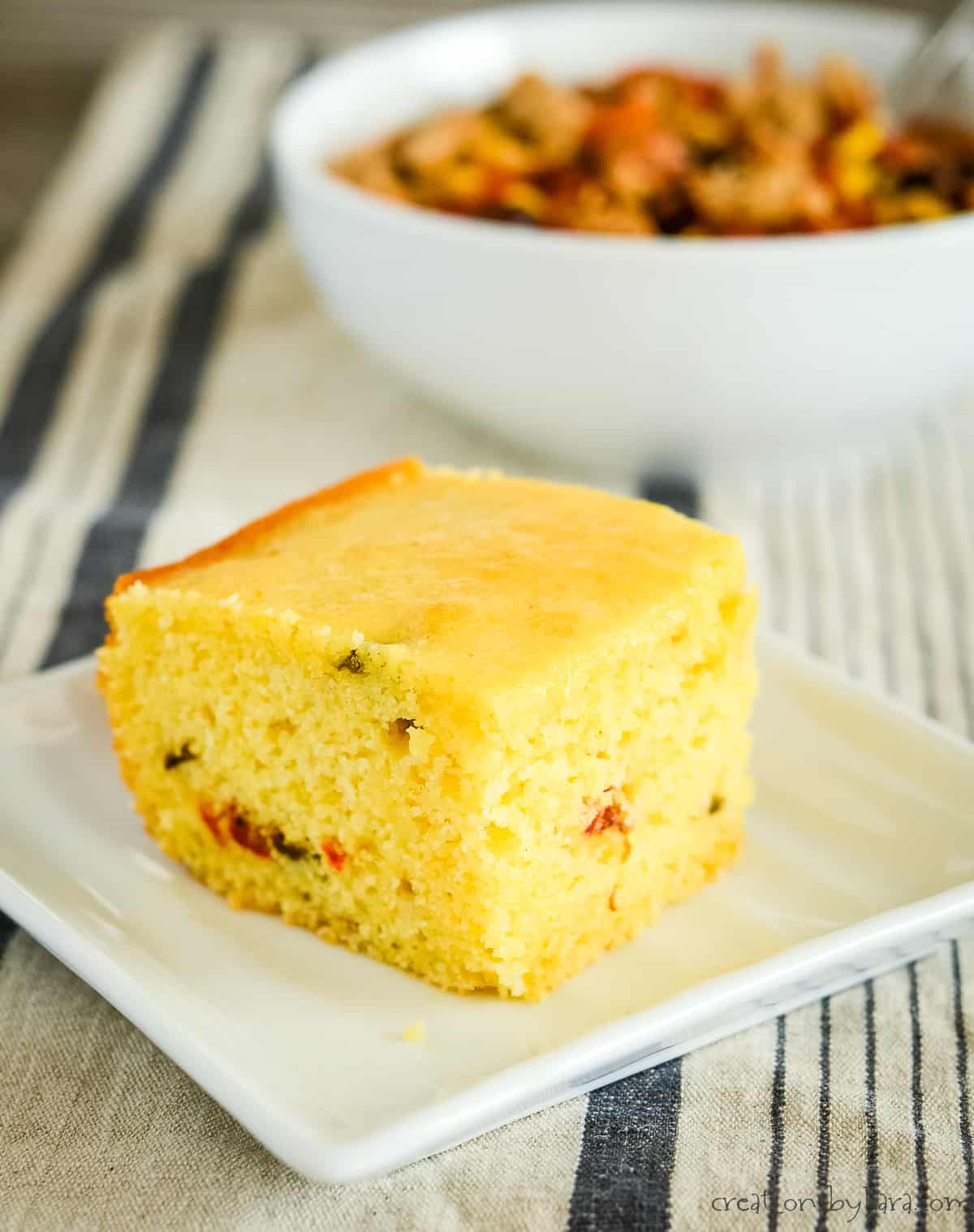 slice of jalapeno cornbread with a bowl of soup in the background