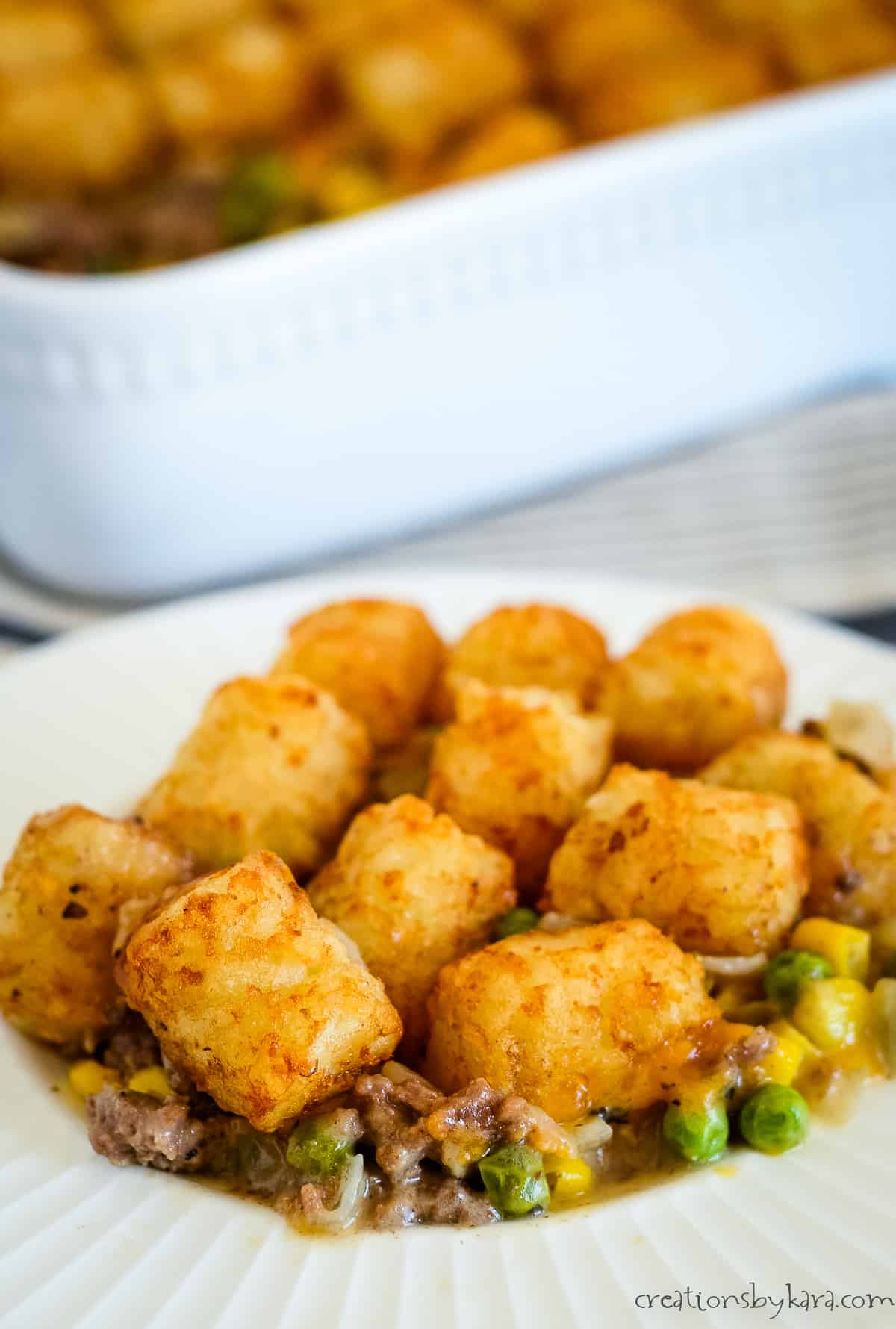 plate of tater tot casserole with a white baking dish in the background