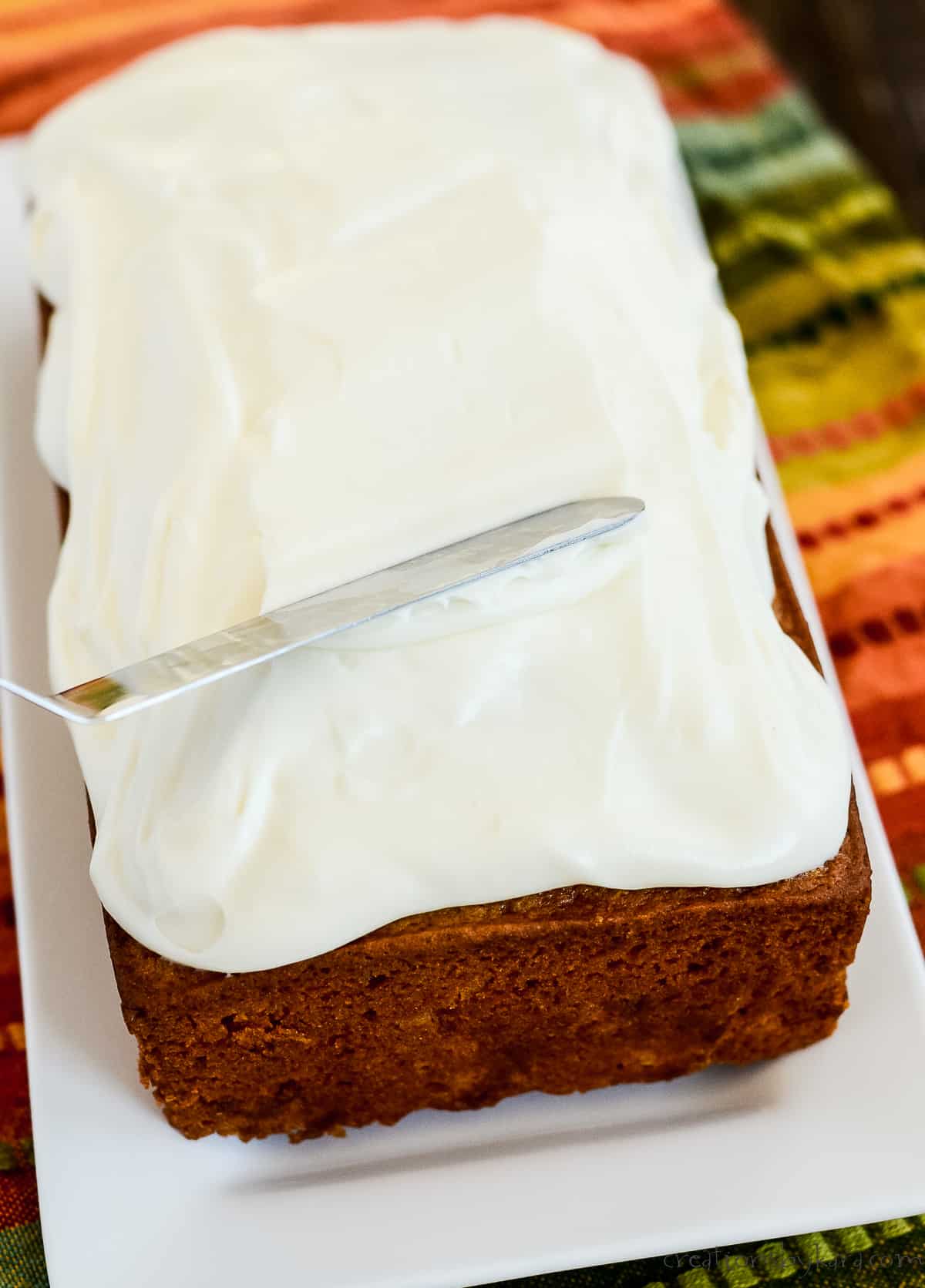frosting being spread on loaf of pumpkin bread