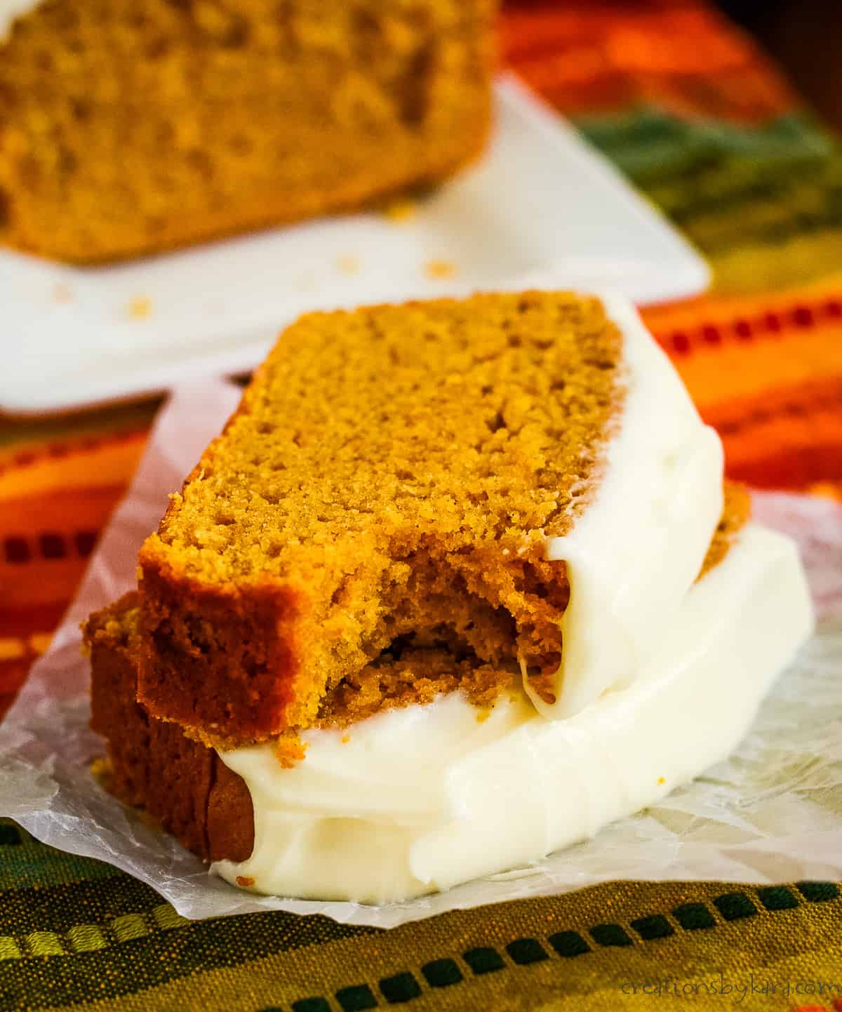 two slices of frosted pumpkin bread, one with a bite taken out of it