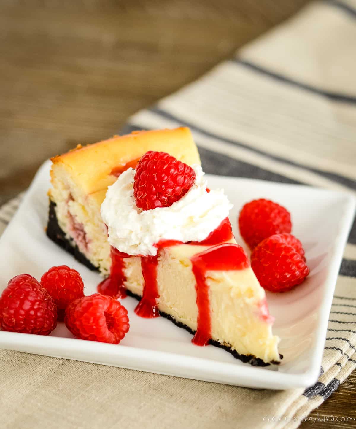 slice of white chocolate raspberry cheesecake on a plate with a whole cheesecake in the background