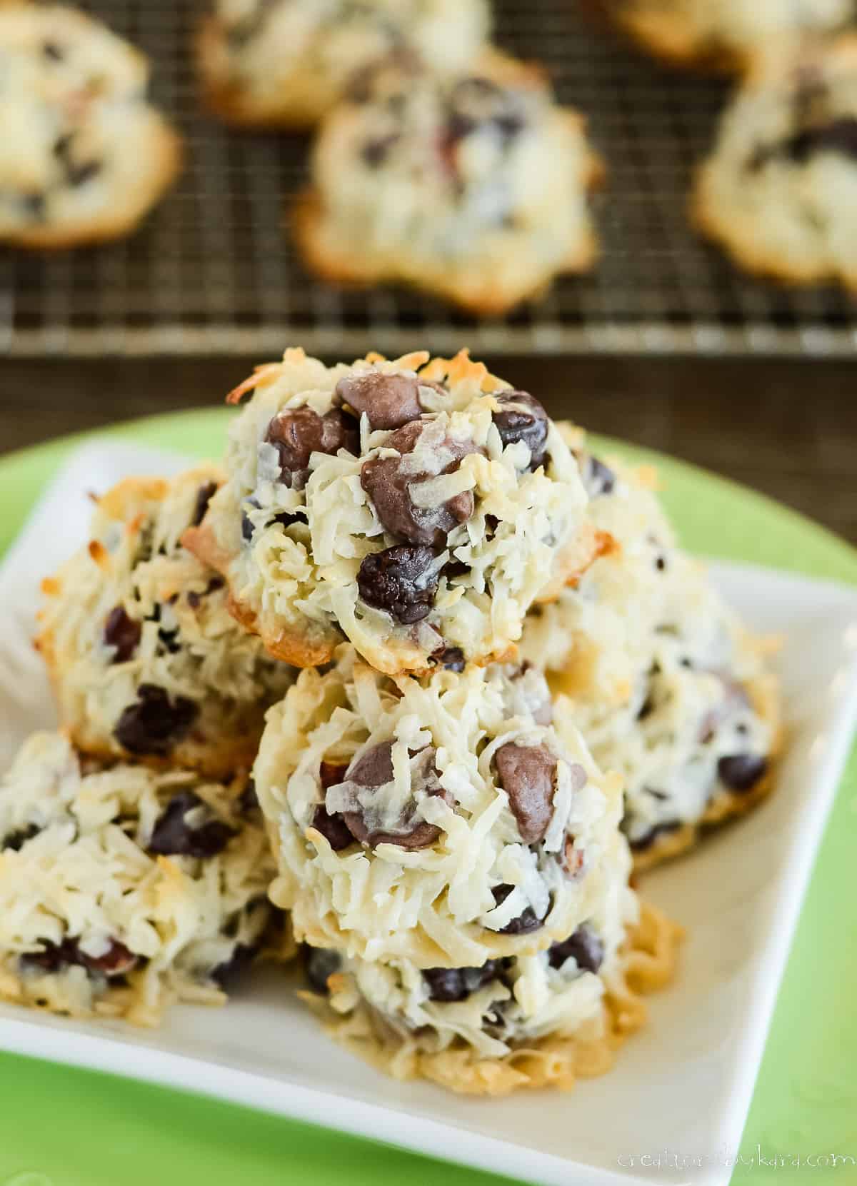 pile of almond joy cookies on a plate with cookies on a wire rack in the background