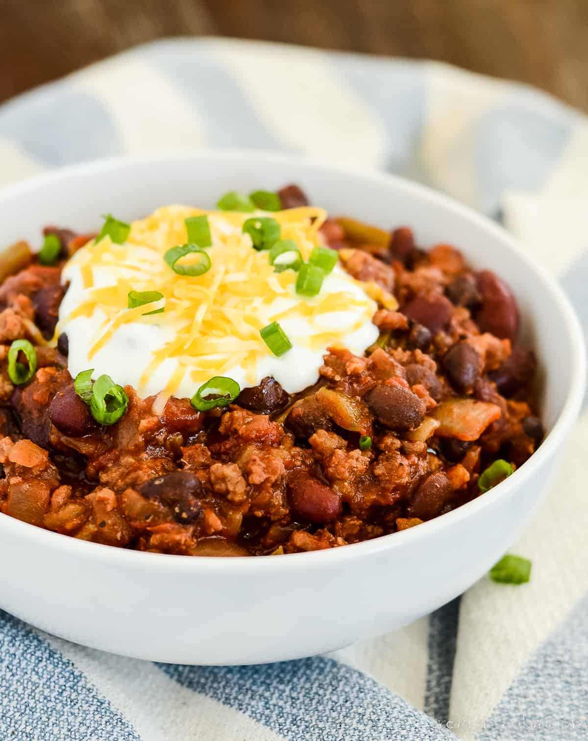 bowl of chili topped with sour cream, shredded cheddar, and green onions