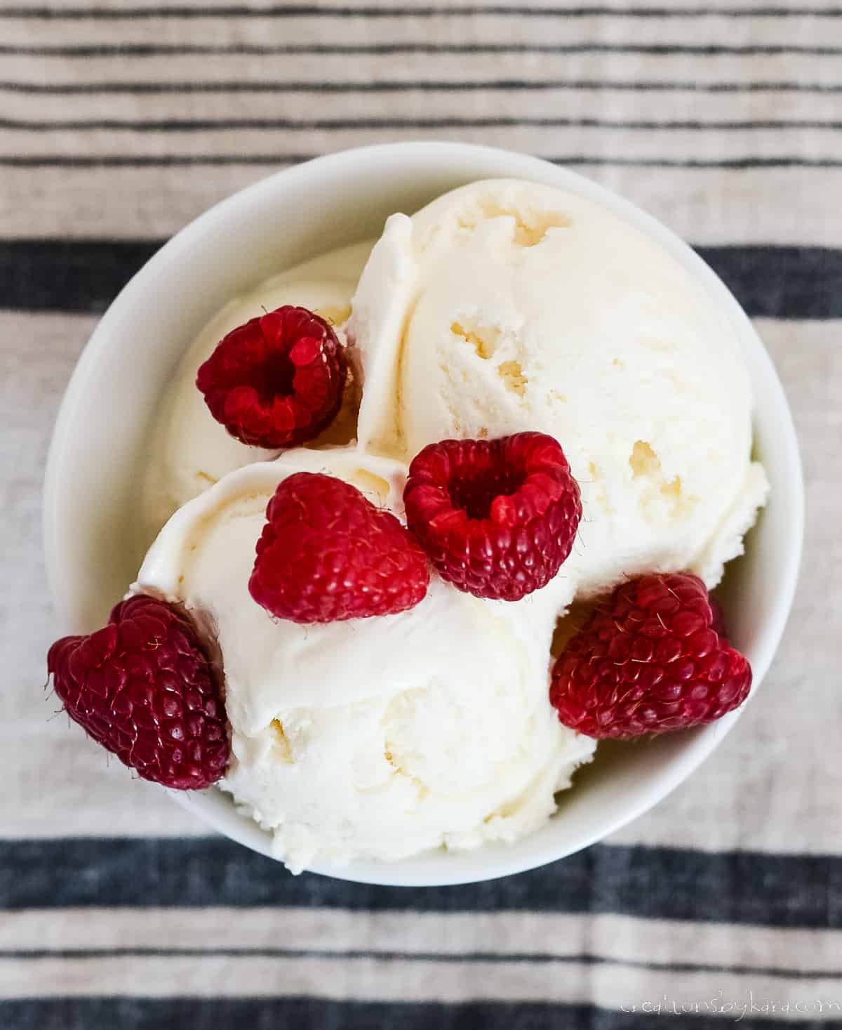 overhead shot of bowl of egg free vanilla ice cream topped with fresh raspberries