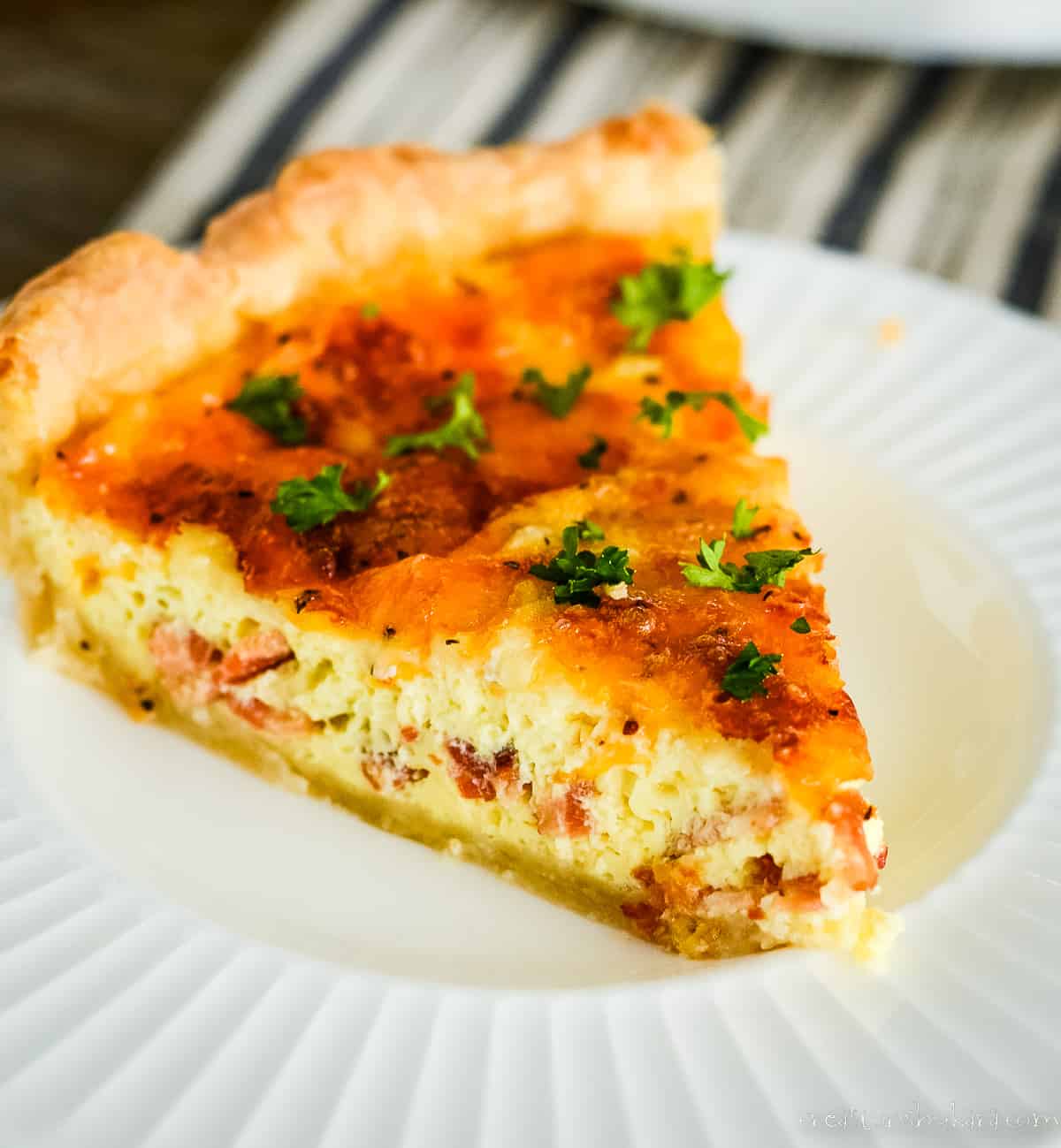 slice of bacon and cheese quiche on a white plate