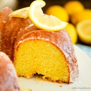 cut lemon pudding cake on a white cake stand with fresh lemons