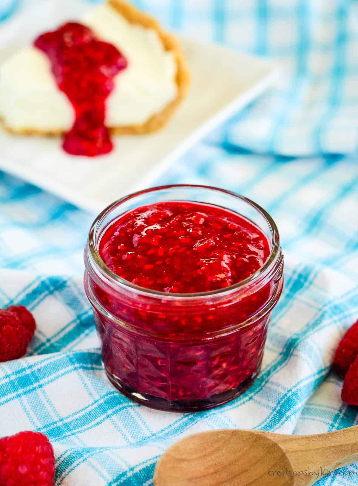 jar of raspberry compote with a slice of cheesecake in the background