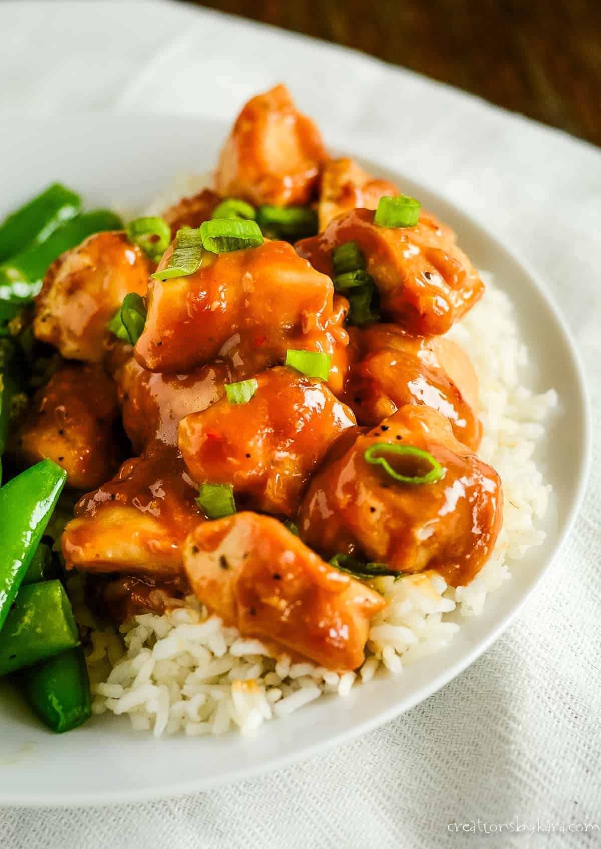 close-up of chicken coated in peanut butter sauce and garnished with green onions