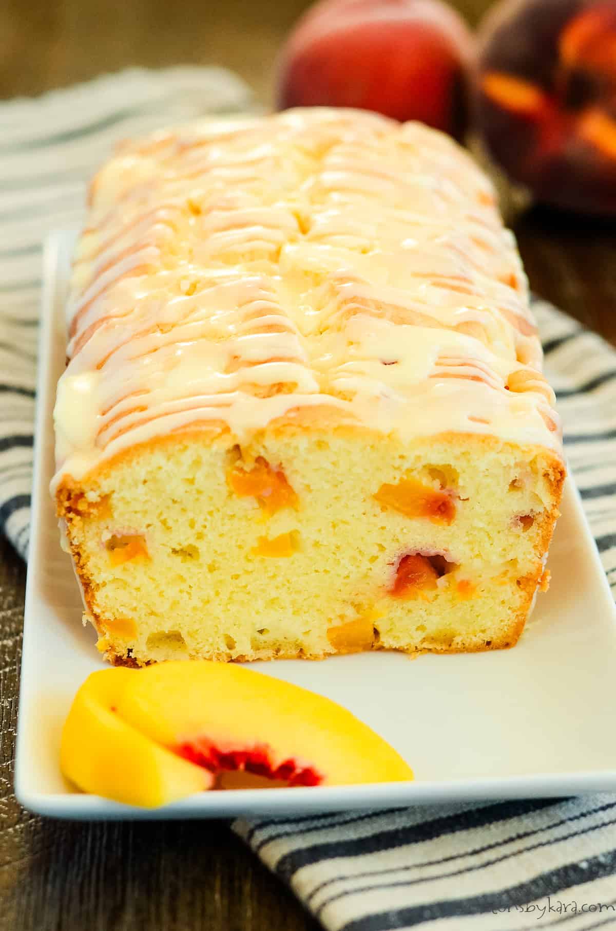 sliced loaf of peach quick bread on a serving plate with slices of peaches