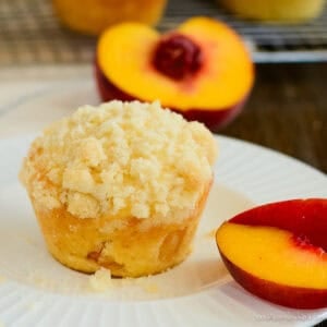 crumb topped peach muffin on a plate with peach slices