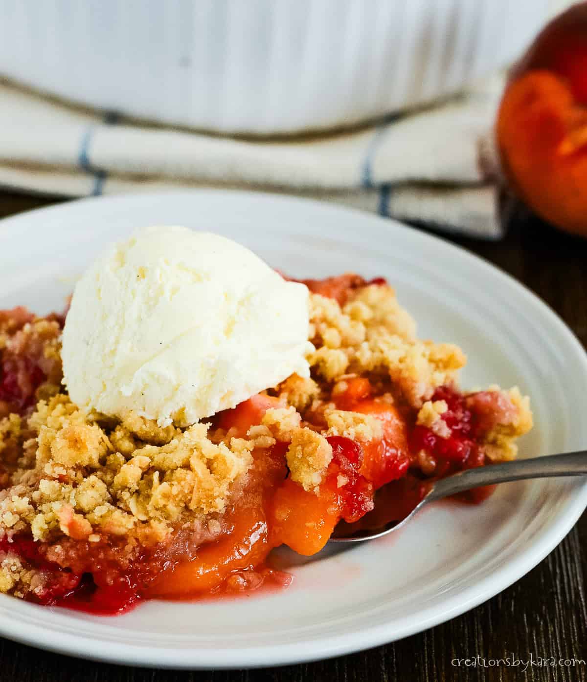 plate of warm raspberry peach crisp with vanilla ice cream and a fork