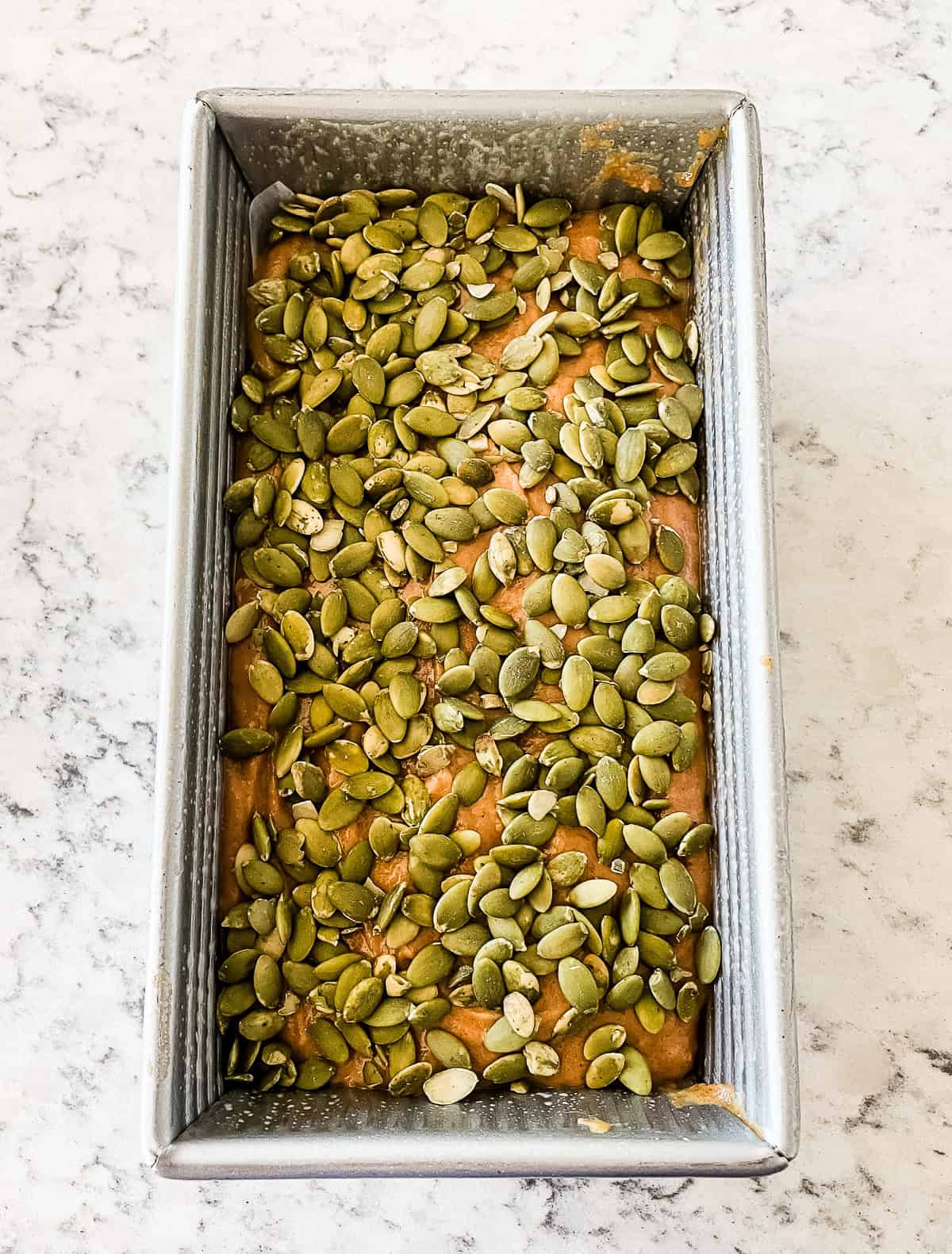 unbaked loaf of pumpkin bread with pepitas on top